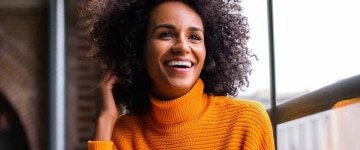 Woman in an orange sweater smiling while looking out the window