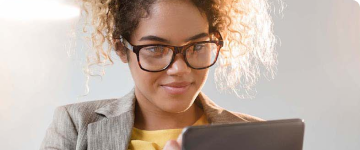 Young woman with glasses looking down at tablet.
