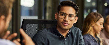 Young professional sitting at a table listening to a coworker