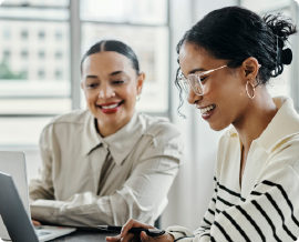 Hispanic woman talking to another woman at a laptop